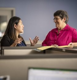 Two researchers at the Marcus Institute for Aging Research in Boston stand next to a cubicle having a discussion.