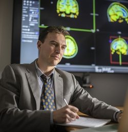 A researcher at the Marcus Institute for Aging Research works at a laptop. Behind him are projected colorful images of a brain MRI scan.