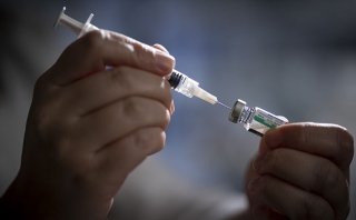 A close-up shot at two hands holding a syringe that is inserted in a vial of medication.