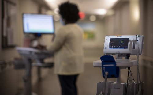 A scene of a hospital floor at Hebrew Rehabilitation Center in Boston, MA, with a nurse standing and working on a computer in the background and a blood pressure monitor in the foreground.