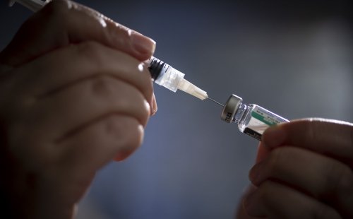 A close-up shot at two hands holding a syringe that is inserted in a vial of medication.
